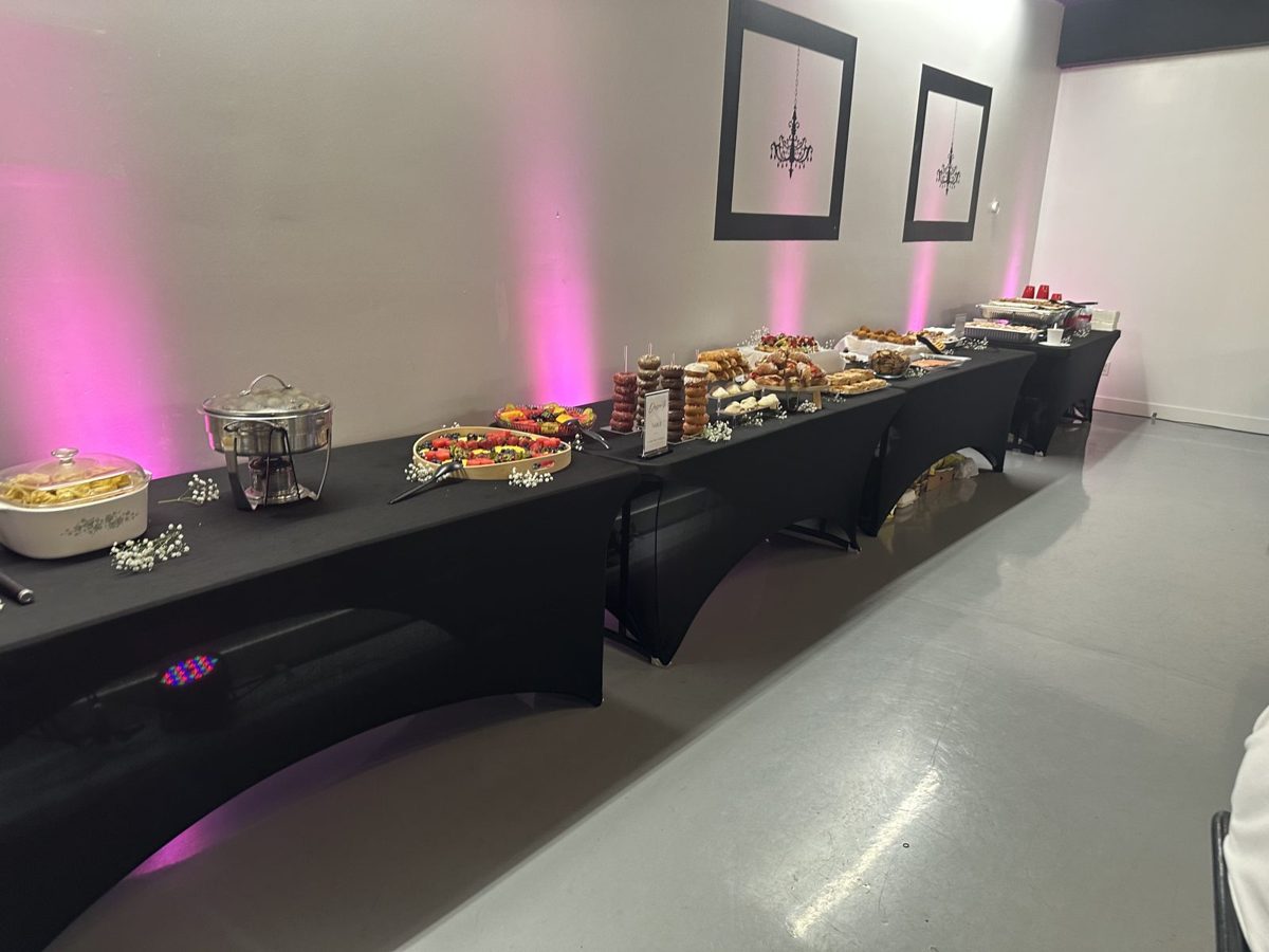 Buffet line of food trays on black-linen tables with pink uplighting