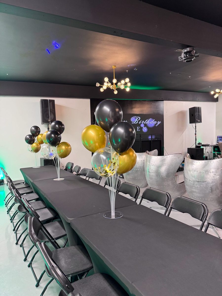 Long black table with black folding chairs and black, gold and white balloon centerpieces