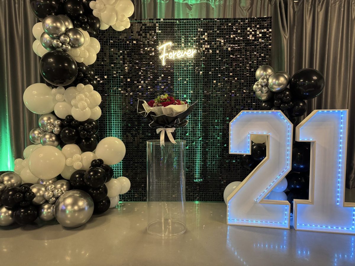 Black, white and silver balloon arch around a sequin backdrop with large light-up 21 numbers
